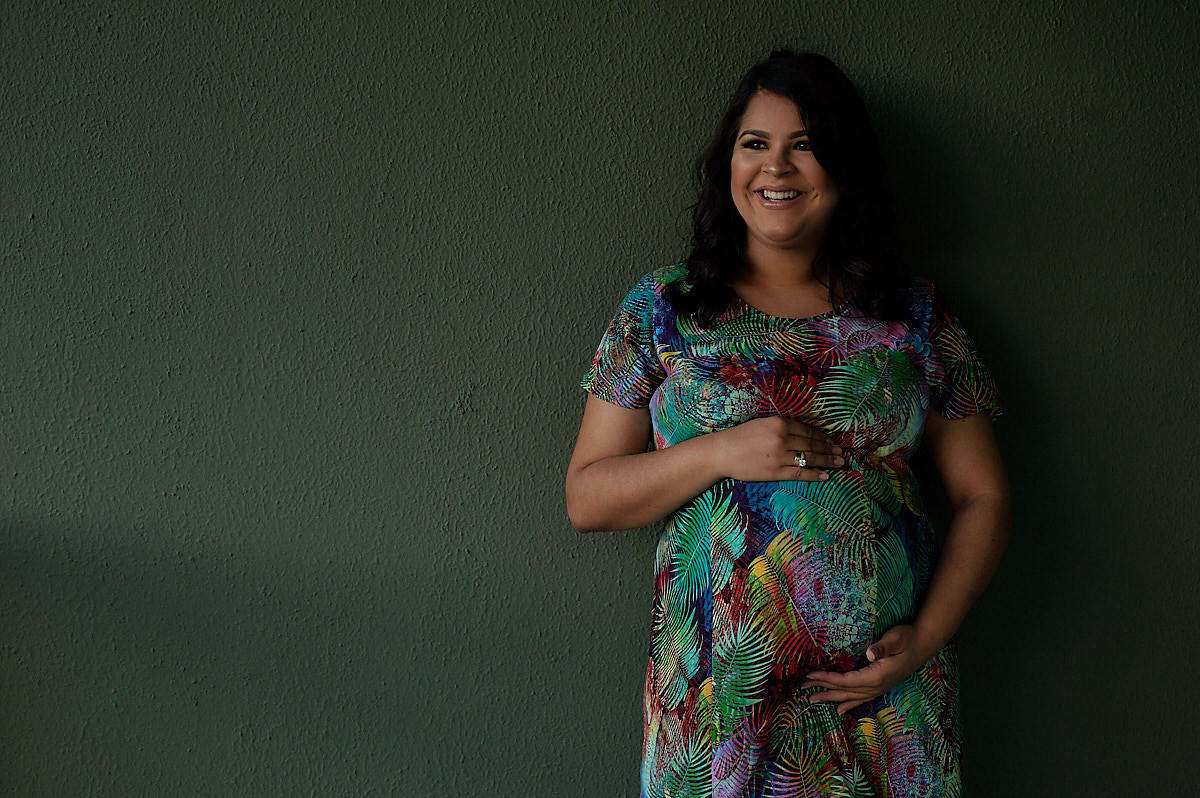 mãe encostada numa parede verde, segurando a barriga