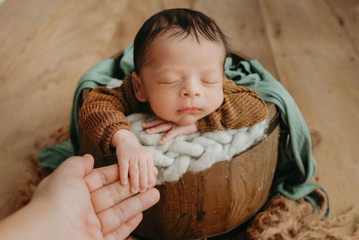 recém nascido com roupa marron dentro de baldinho dando as mãos para a mamãe
