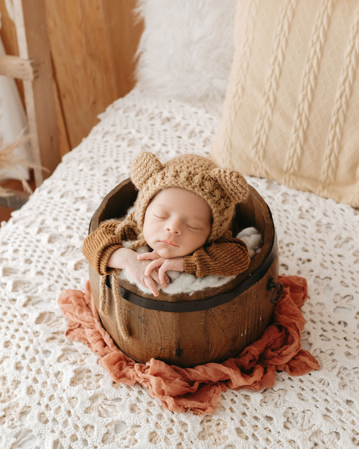 recém nascido dentro de baldinho em cima de uma cama com manta rústica