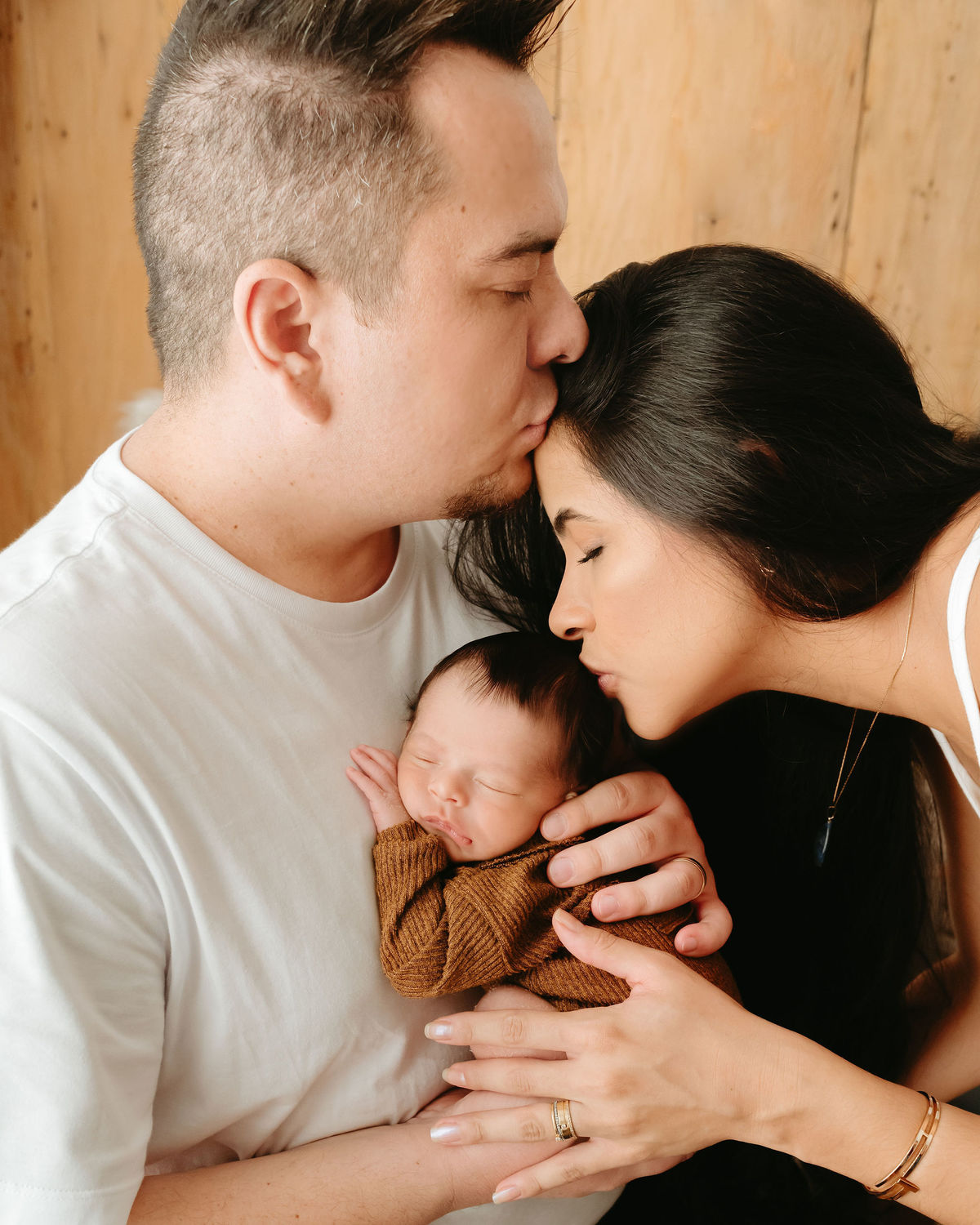 pai segurando seu bebe e mãe dando um beijo na cabeça do recém nascido