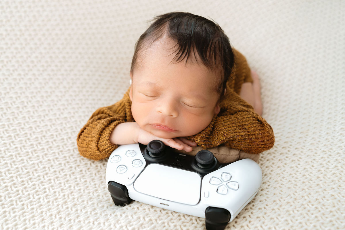 bebê recem nascido com braços em cima de um controle remoto de video game