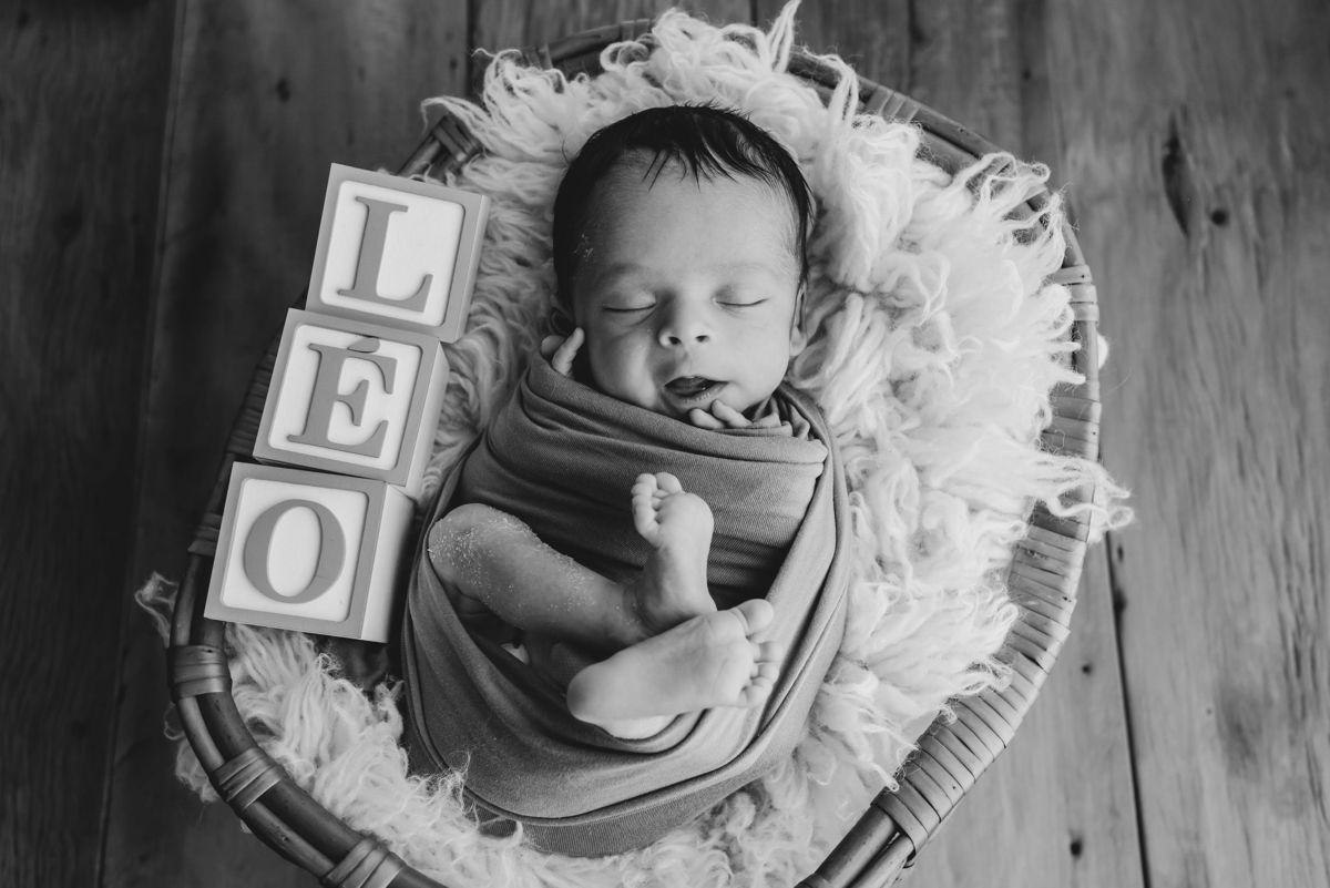 bebe enrolado em cesto de vime com cubos escrito LEO
