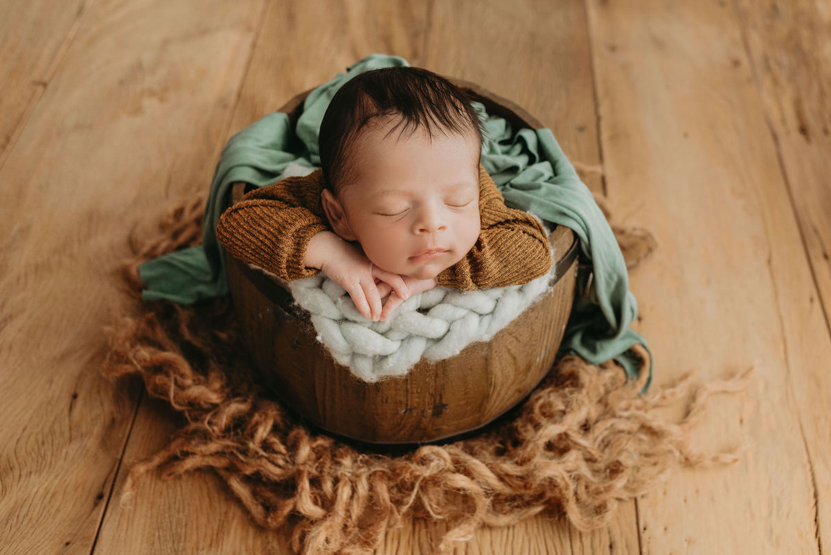 bebe com roupa marron dentro de um baldinho com braço na borda