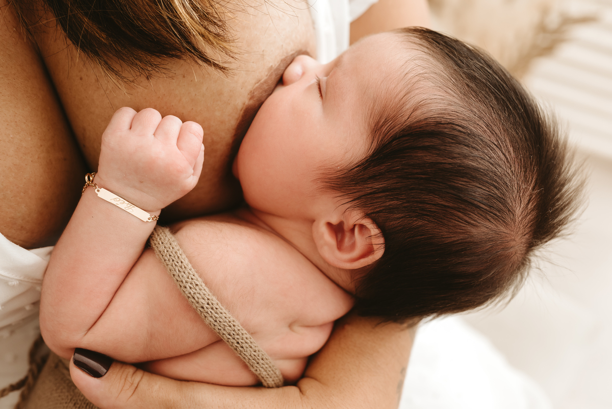bebe mamando. no pulso, uma pulseira com seu nome gravado: Leonardo