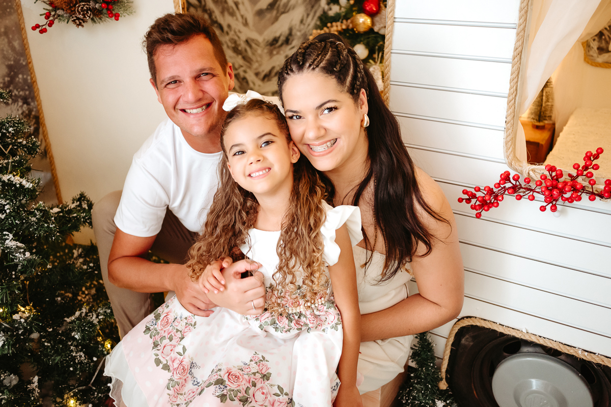 familia sorrindo em cenário natalino mãe, pai e filha