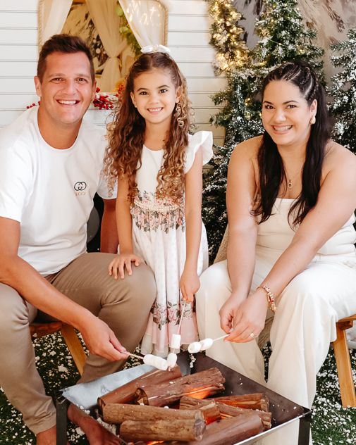 família sentada em frente a uma fogueira assando marshmallows de natal