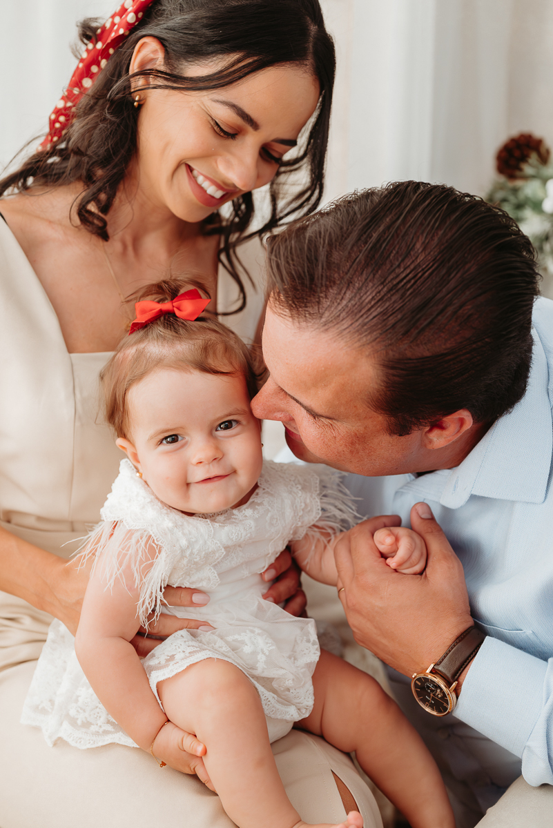 pai dando beijinho no rosto da sua filha que esta olhando para mim. mae esta sentada com filha no colo