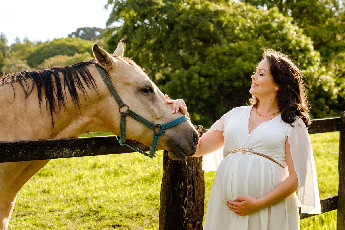 gestante usando vestido branco passando a mão em um cavalo