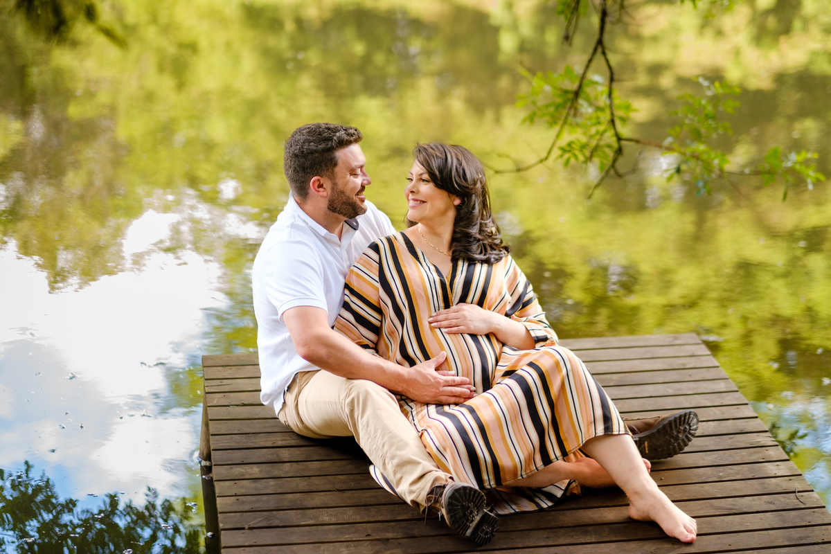 gestante com o marido na beira do lago sentada no deck
