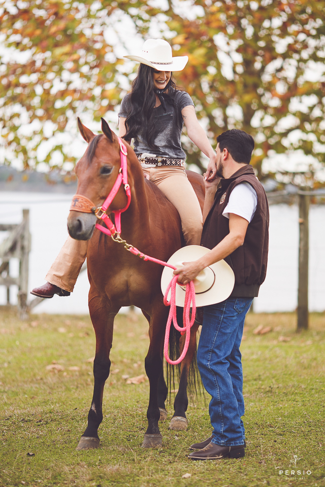 casal se olhando fazendo fotos com cavalos na chacara capela das graças em araucaria parana ensaio com os fotografos persio photo art com o noivo beijando a mão da noiva