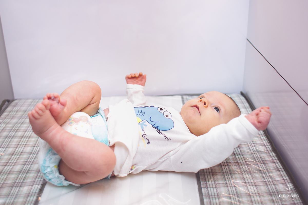 bebe lindo com os braços abertos deitado no trocador no ensaio newborn estilo life style da fotografa raphaela persio persio photo art