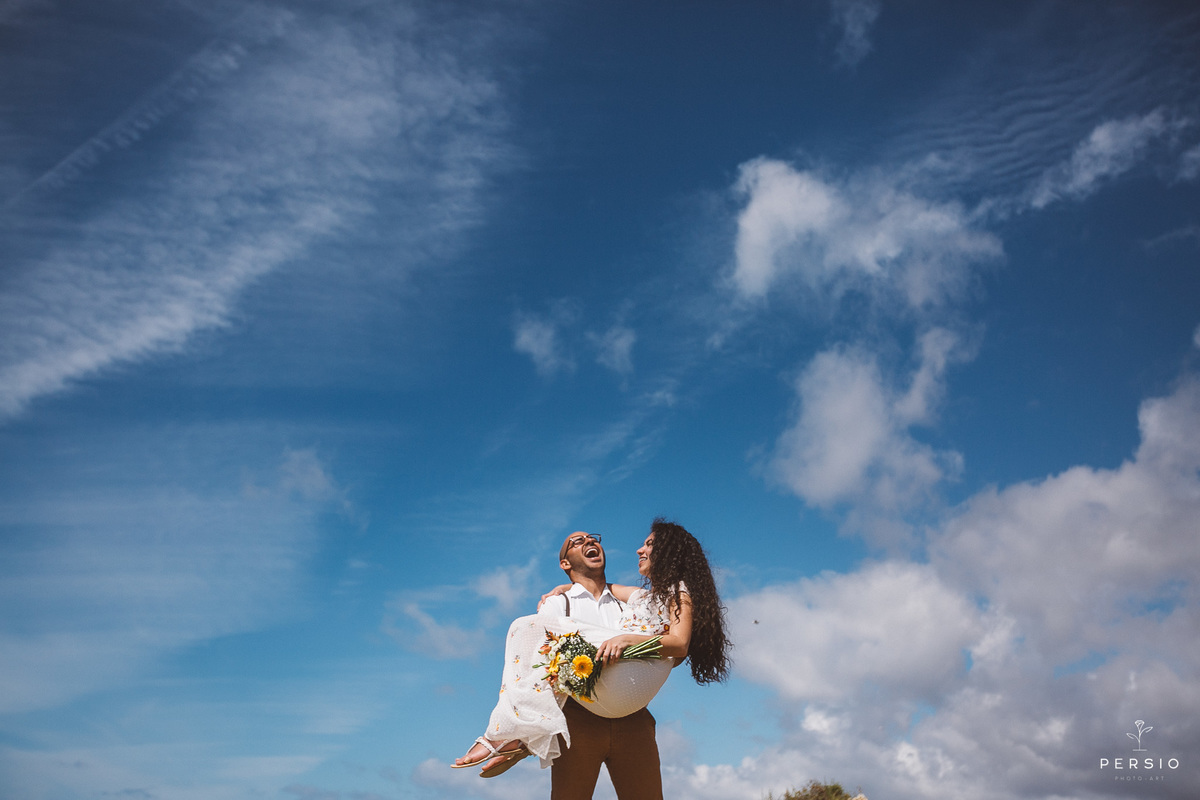 noiva no colo do noivo sorrindo e céu azul ensaio pre wedding em portugal