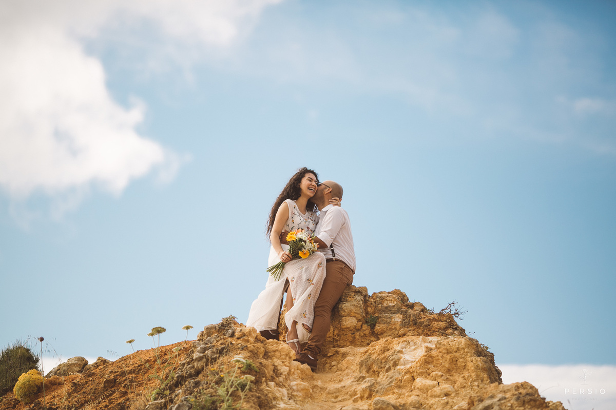 noivo beijando a noiva sorridente em uma montanha na praia de Lagos Portugal