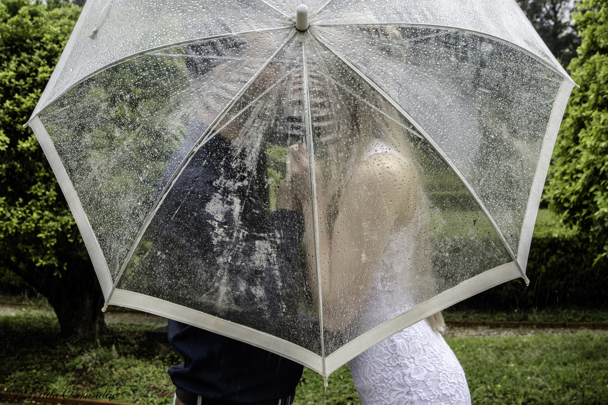 Ensaio de casal na chuva, guarda chuva transparente faz pano de fundo para o beijo do casal. parque da independencia SP
