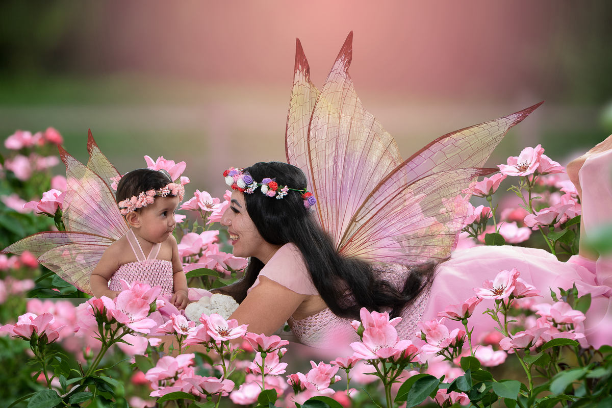 Ensaio fotográfico lúdico com tema Jardim encantado, mãe segurando a filha com asas de fada