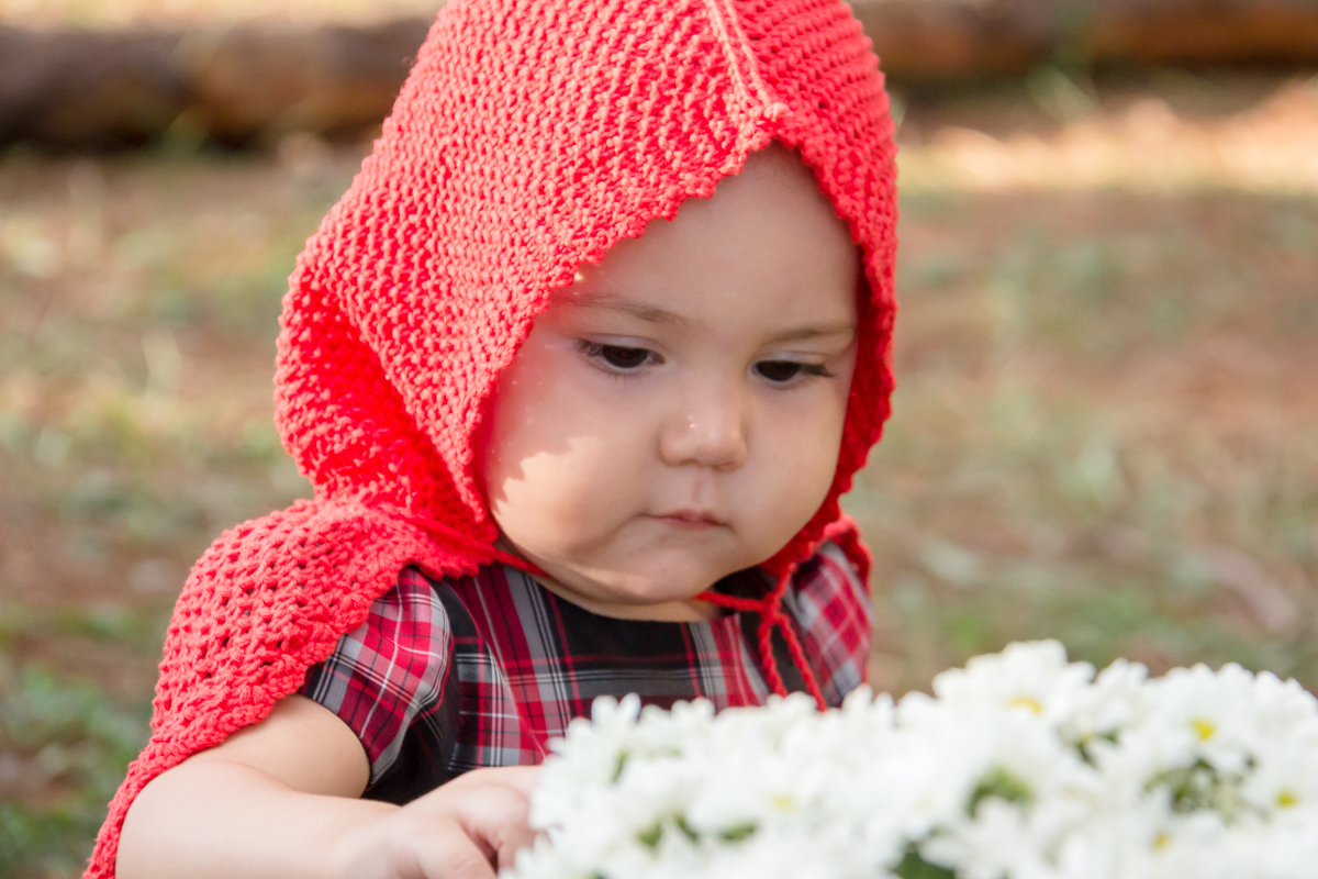 Bebê de chapeuzinho vermelho vendo as flores margaridas