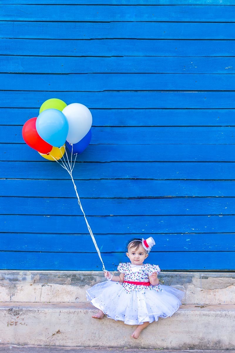 fundo azul menina bebê segura balões coloridos