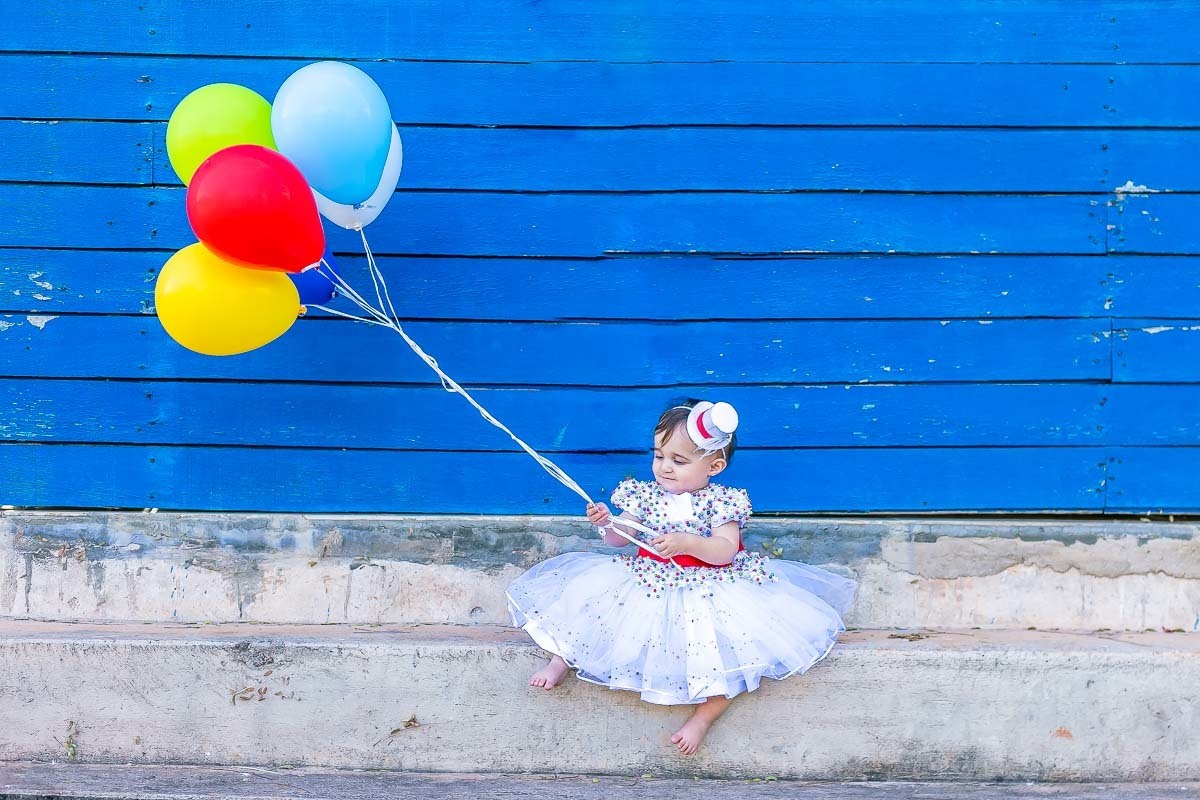 fundo azul criança segura balões coloridos