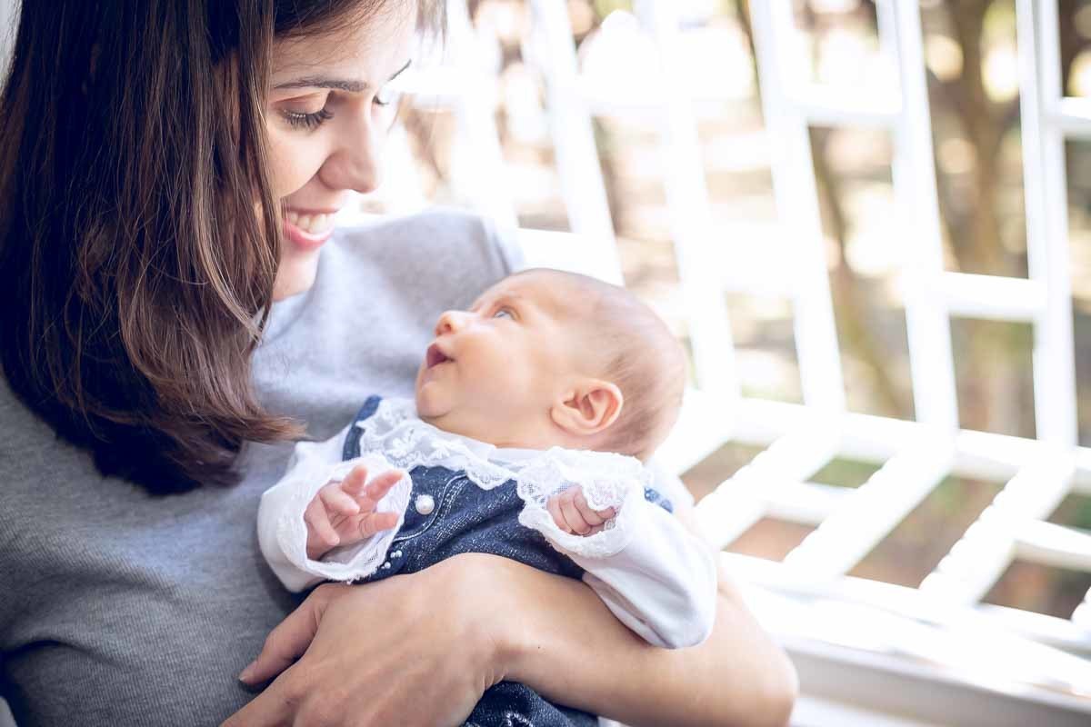 mãe olhando a bebê em frente a janela