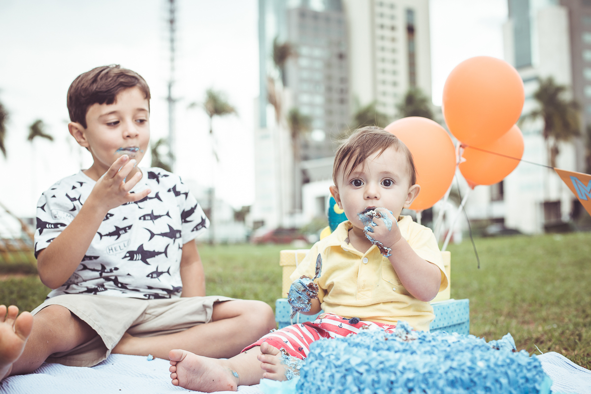 ensaio smash the cake tema foguete primeiro aninho parque da cidade família laranja e azul banho menino  Brasília DF veloso valentim book família fotografia bebê e irmão comendo bolo