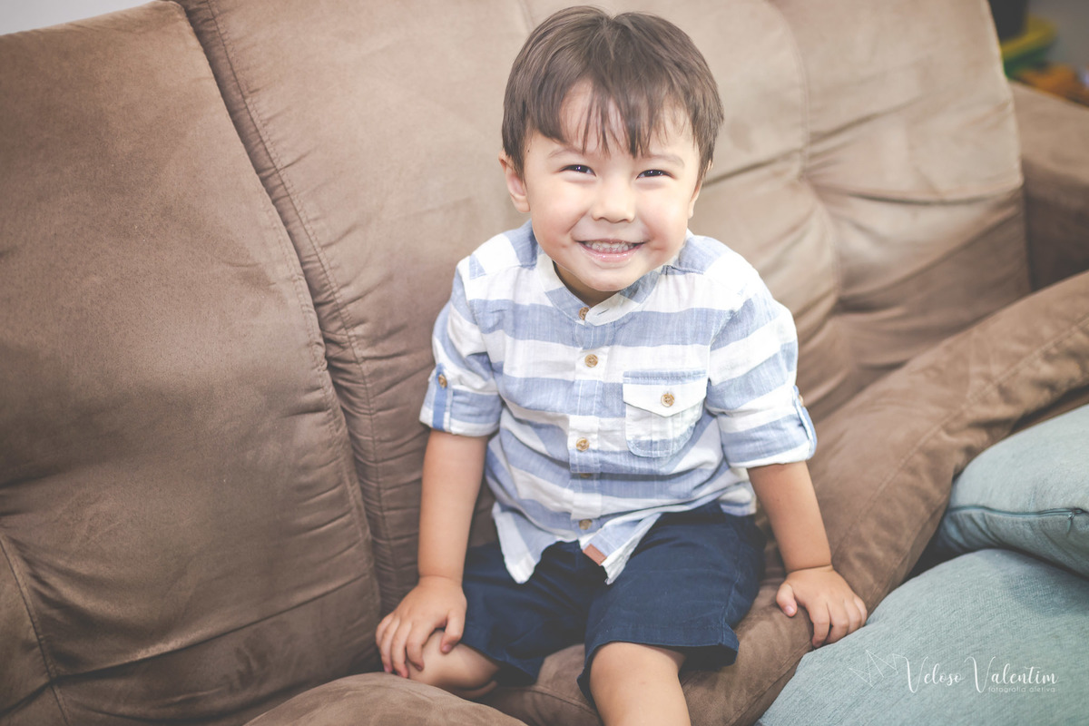 ensaio acompanhamento do primeiro ano do bebê Laura 3 meses em casa com a família ensaio lifestyle cotidiano Brasília DF Veloso Valentim fotografia afetiva irmão mais velho no sofá criança sorrindo menino oriental