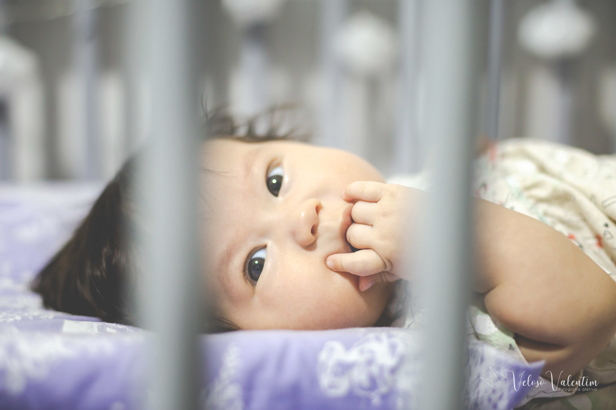 ensaio acompanhamento do primeiro ano do bebê Laura 3 meses em casa com a família ensaio lifestyle cotidiano Brasília DF Veloso Valentim fotografia afetiva bebê no berço com a mão na boca menina oriental