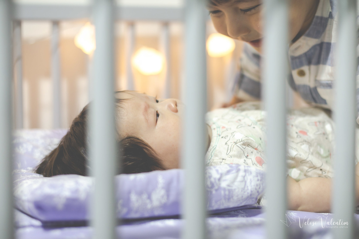 ensaio acompanhamento do primeiro ano do bebê Laura 3 meses em casa com a família ensaio lifestyle cotidiano Brasília DF Veloso Valentim fotografia afetiva bebê no berço com irmão mais velho menina oriental