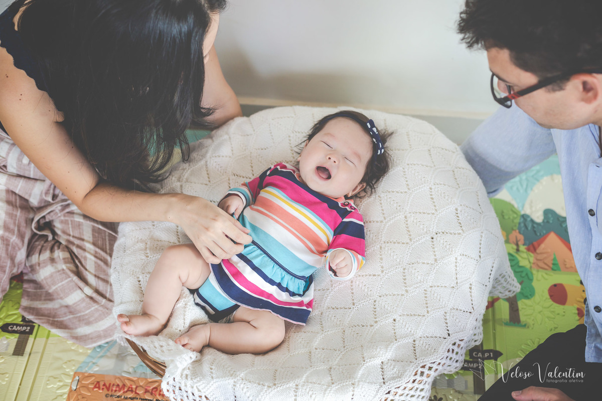 ensaio acompanhamento do primeiro ano do bebê Laura 3 meses em casa com a família ensaio lifestyle cotidiano Brasília DF Veloso Valentim fotografia afetiva família oriental pai e mãe olham a bebê deitada