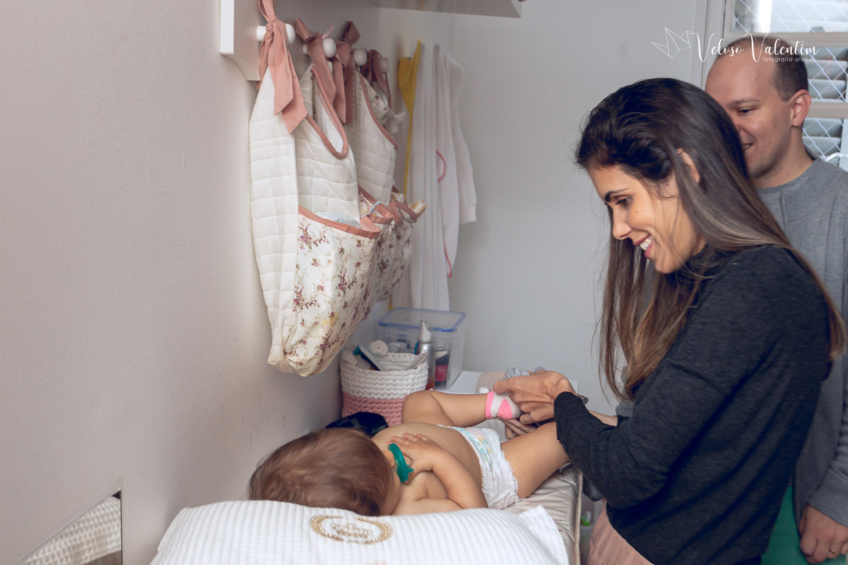 ensaio acompanhamento do primeiro ano do bebê Aurora 12 meses em casa com a família ao ar livre aprendendo a andar primeiros passos Brasília DF Veloso Valentim fotografia afetiva pais trocando a fralda da bebê