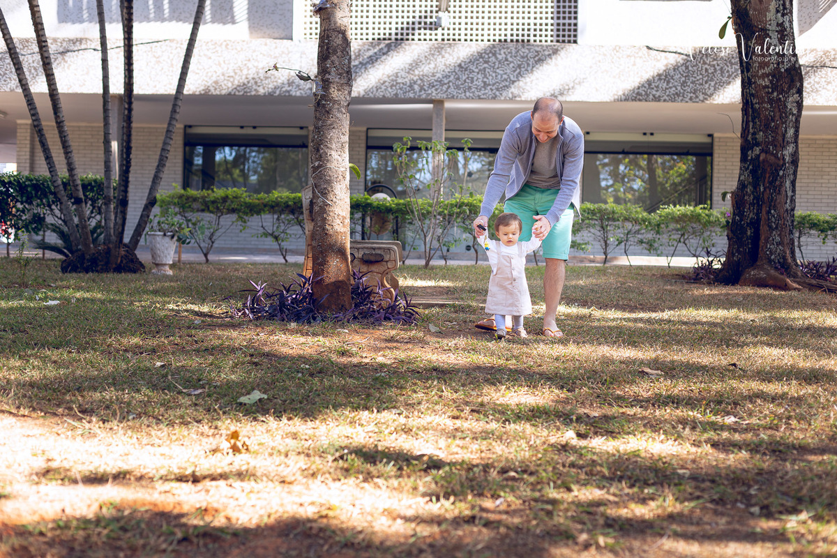 ensaio acompanhamento do primeiro ano do bebê Aurora 12 meses em casa com a família ao ar livre aprendendo a andar primeiros passos Brasília DF Veloso Valentim fotografia afetiva bebê andando na grama com o pai