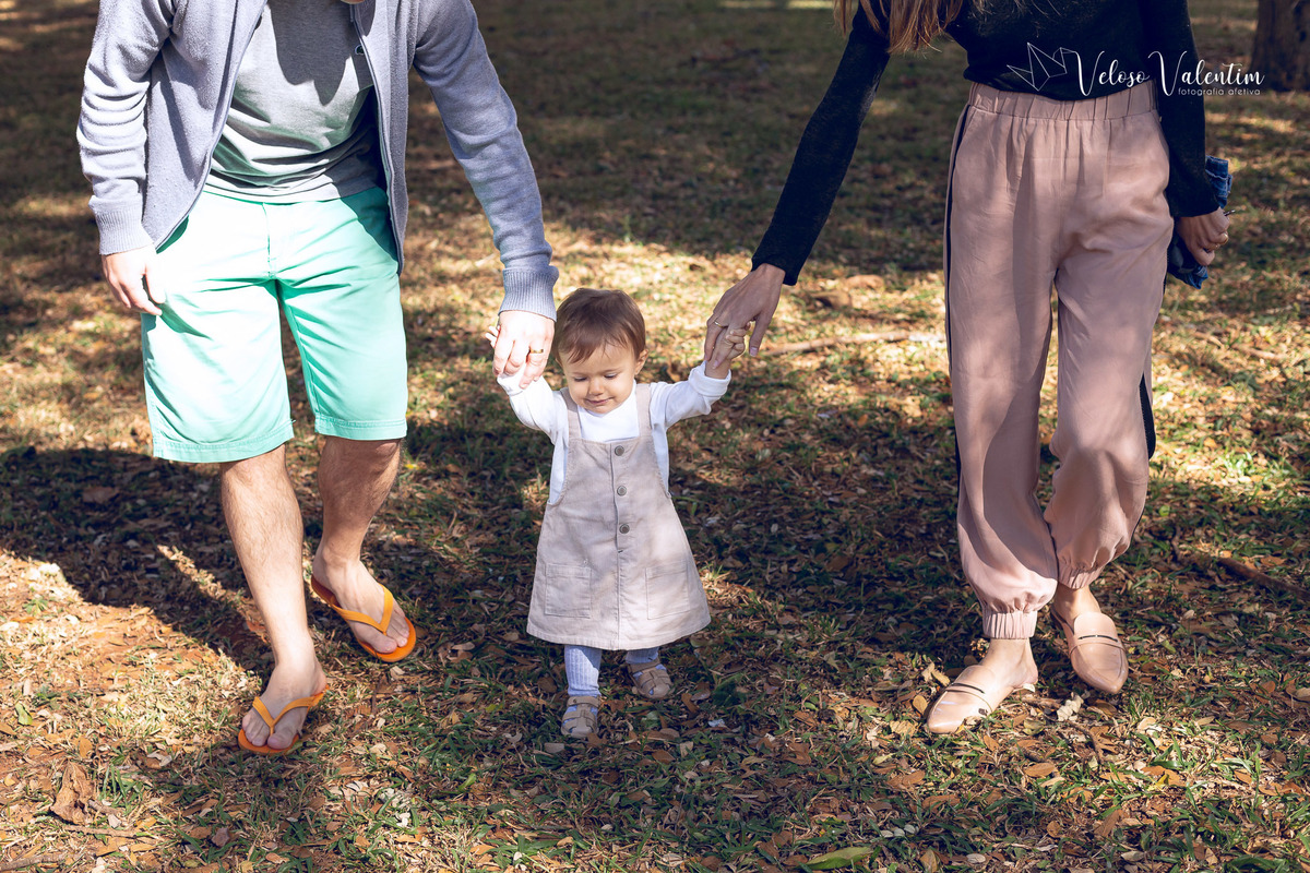 ensaio acompanhamento do primeiro ano do bebê Aurora 12 meses em casa com a família ao ar livre aprendendo a andar primeiros passos Brasília DF Veloso Valentim fotografia afetiva bebê andando na grama com os pais