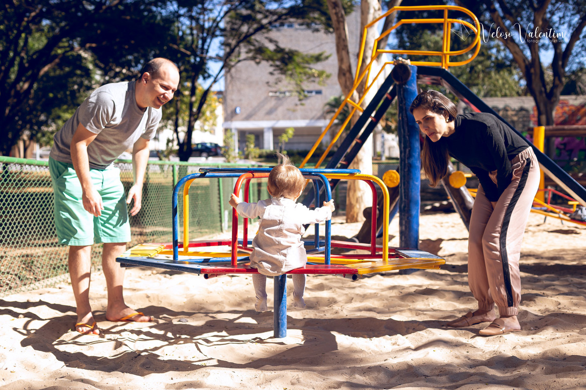 ensaio acompanhamento do primeiro ano do bebê Aurora 12 meses em casa com a família ao ar livre aprendendo a andar primeiros passos Brasília DF Veloso Valentim fotografia afetiva bebê no balanço do parquinho com o pai com os pais