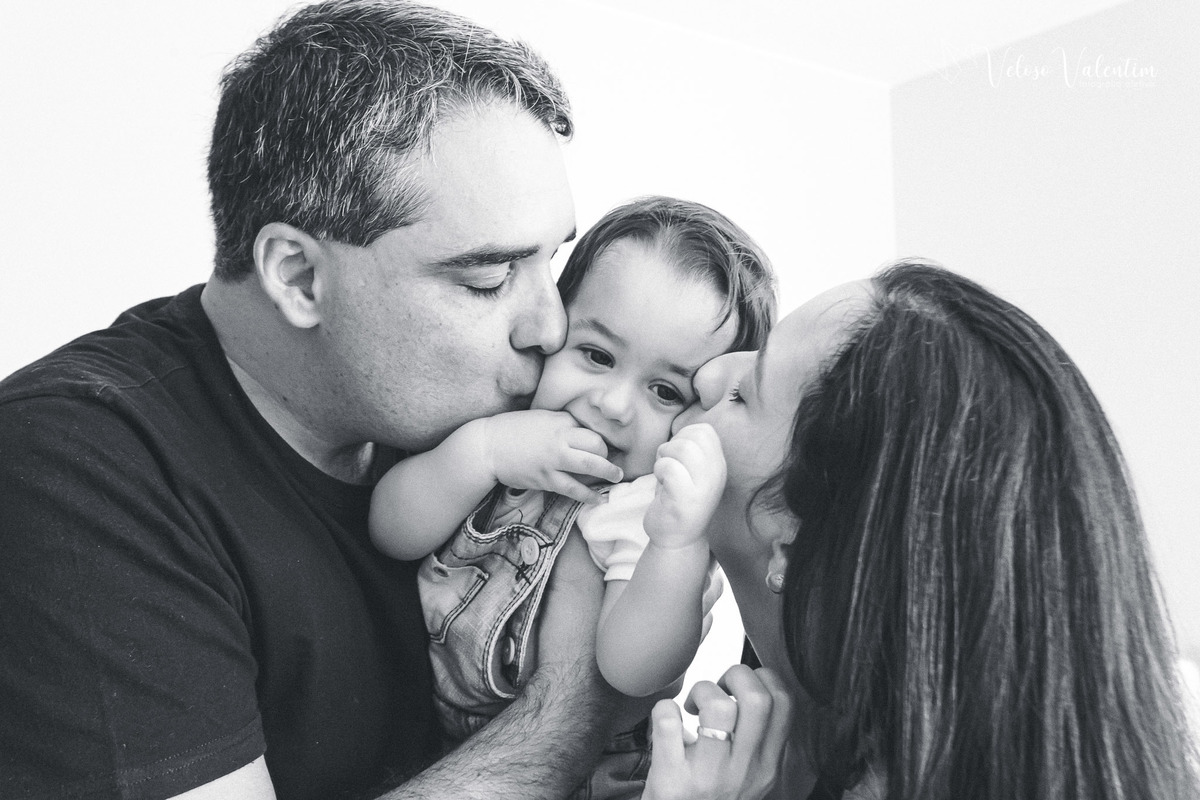 ensaio acompanhamento do primeiro ano do bebê Gabriel 12 meses em casa com a família ao ar livre engatinhando pai mãe avós ensaio família acompanhamento mensal fotográfico Brasília DFpais beijando o bebê foto em preto e branco