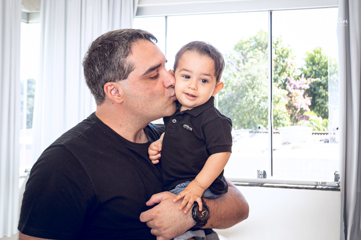 ensaio acompanhamento do primeiro ano do bebê Gabriel 12 meses em casa com a família ao ar livre engatinhando pai mãe avós ensaio família acompanhamento mensal fotográfico Brasília DF colo e beijo do pai 