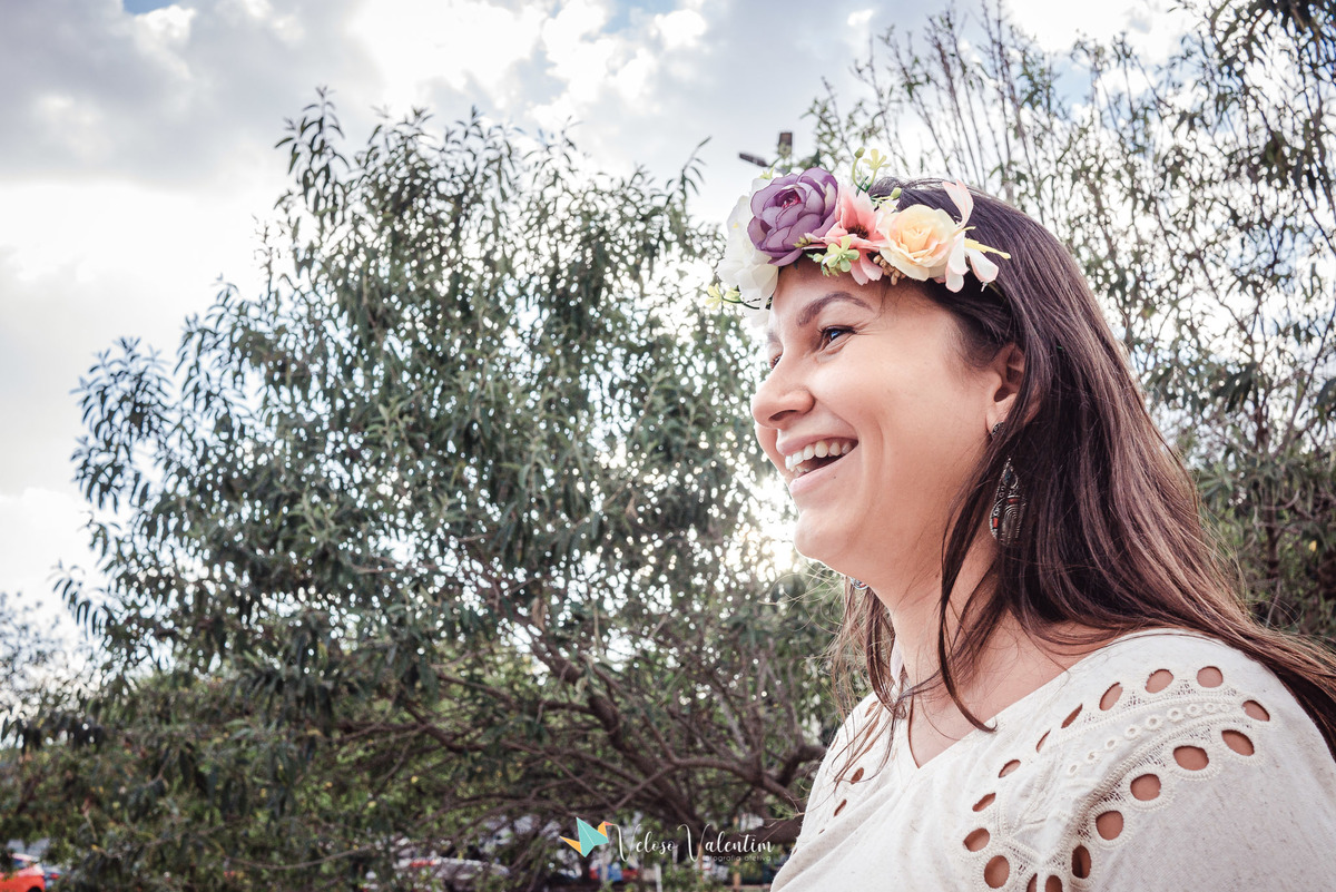 mulher sorrindo com coroa de flores com árvores ao fundo
