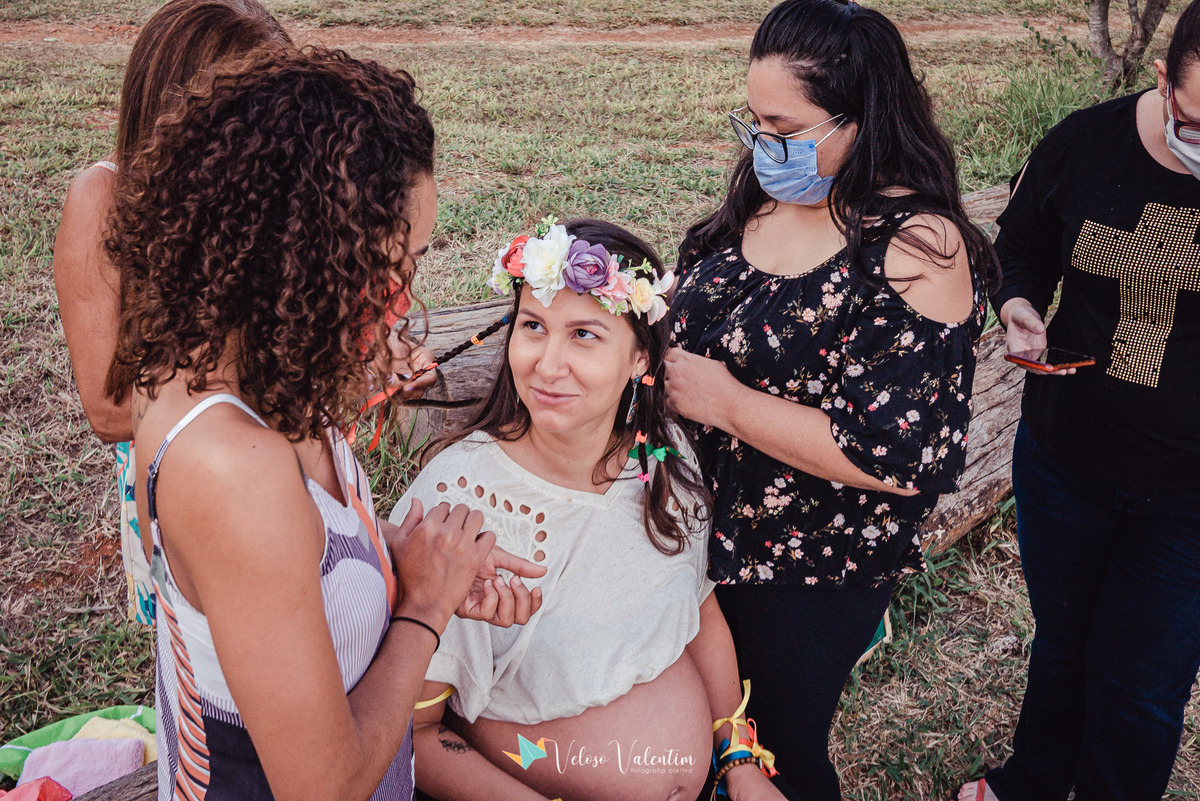 mulheres trançam o cabelos de uma mulher grávida com coroa de flores