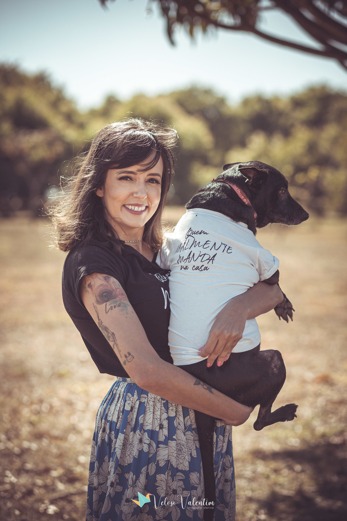 mulher com cachorro preto no colo, cachorro veste uma camiseta branca
