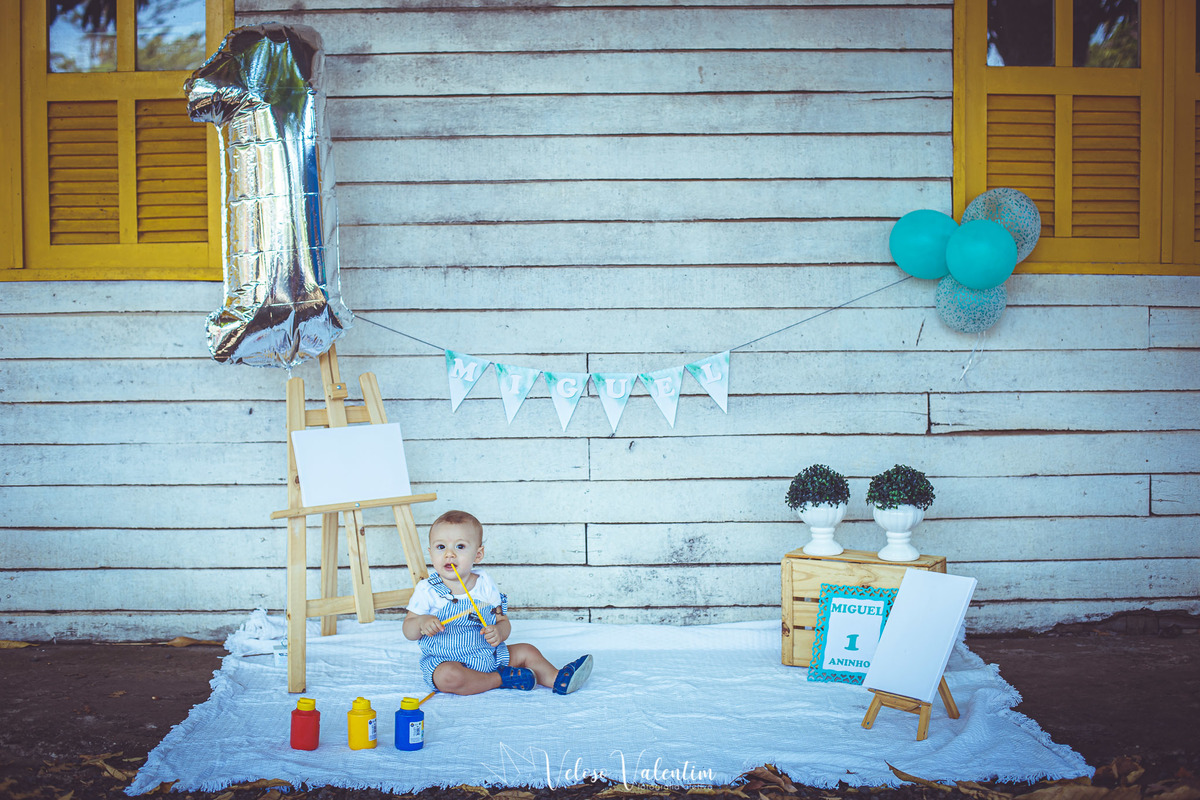 bebê sentado numa toalha no chão com cenário com tintas