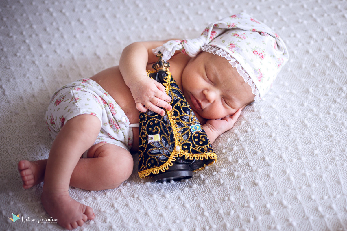 bebê deitada dormindo abraçada a uma imagem de nossa senhora ensaio newborn em casa Brasília