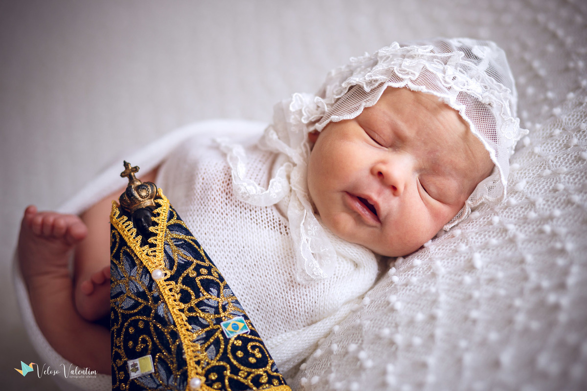 bebê deitada dormindo ao lado de uma imagem de nossa senhora ensaio newborn em casa Brasília