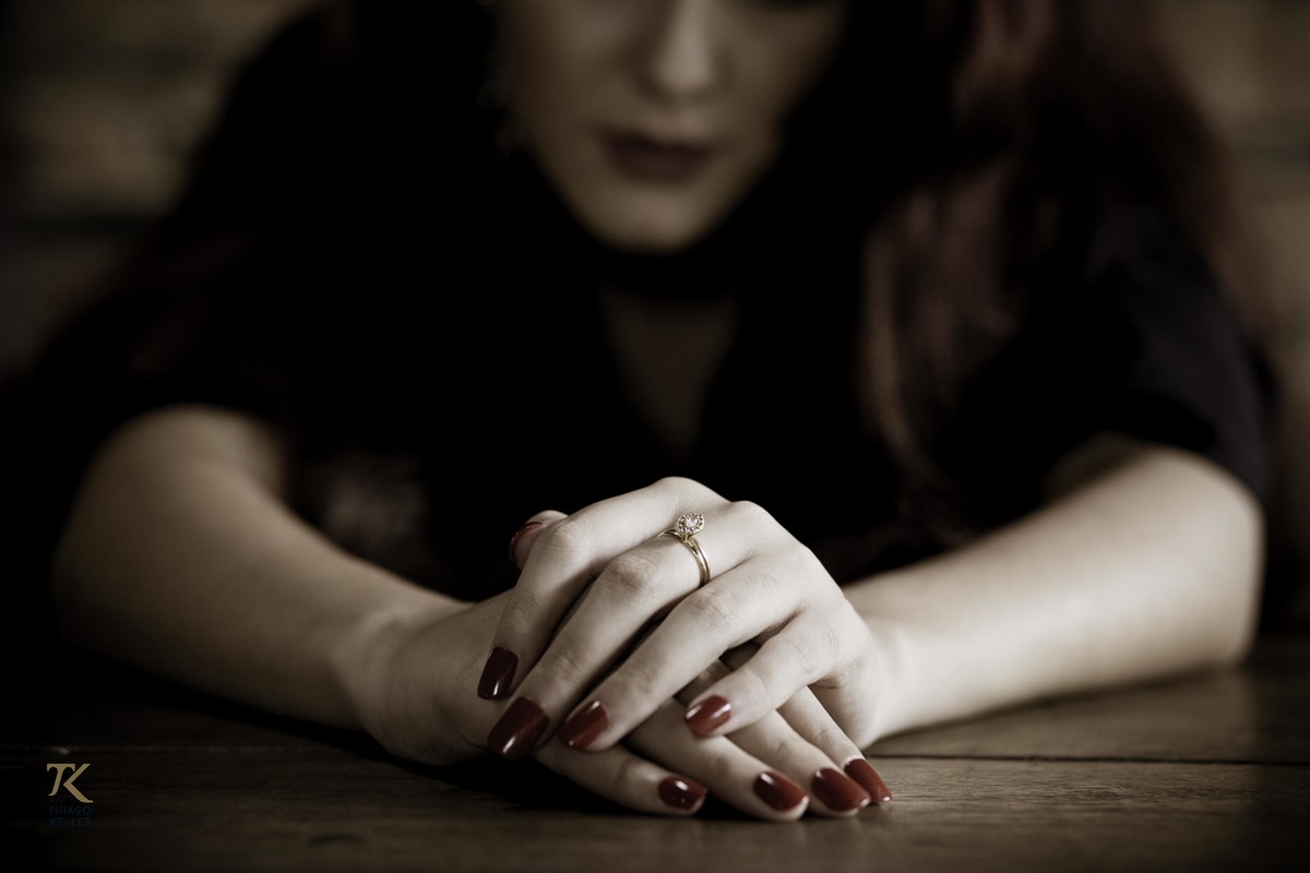 Sessão Fotográfica com Ana Lima, realizado em Minas Gerais. Foto da modelo sentada na mesa. Detalhe do anel. Observação.