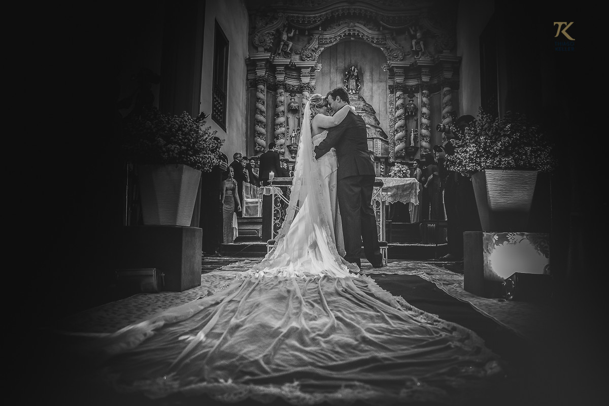Foto em preto e branco ao final da cerimônia de casamento. Noivo e noiva dão o seu primeiro beijo casados.
