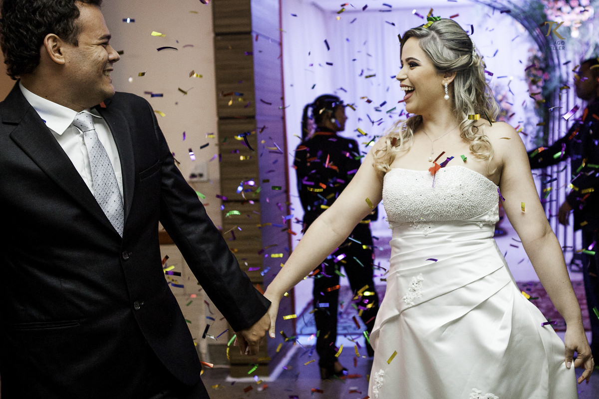Noivo e noiva entram na festa felizes, com confetes. Foto divertida e leve.