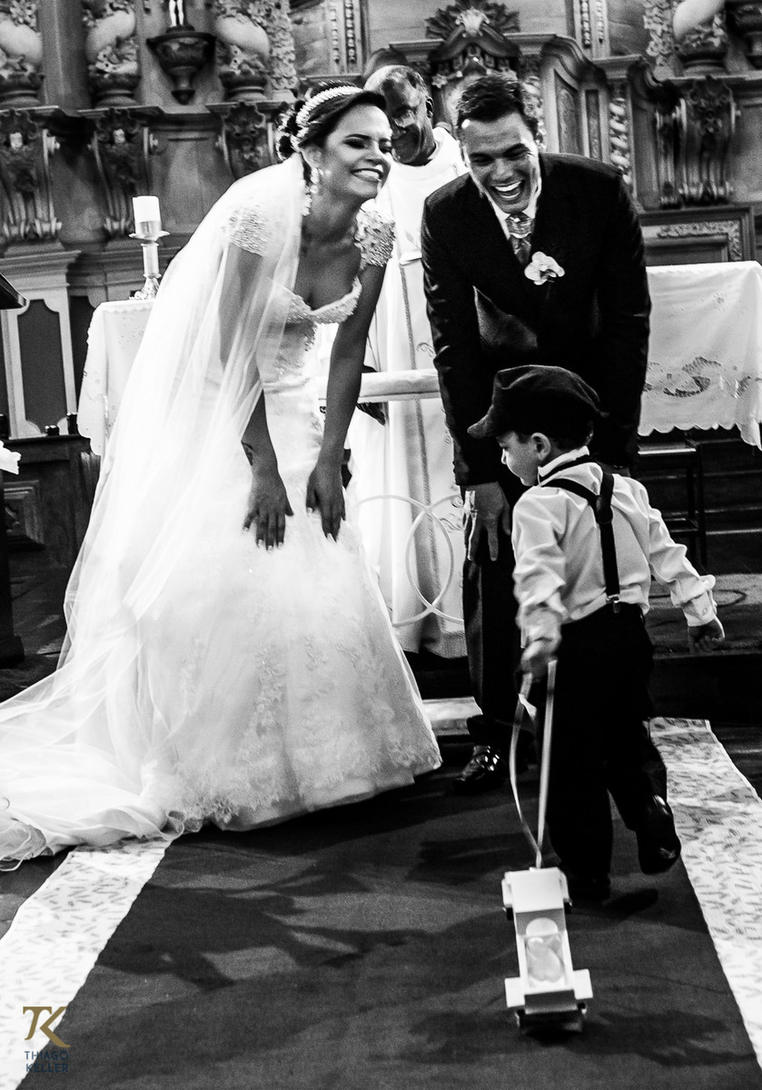 Casamento de Sabrina e Alisson. Noivos sorriem ao ver o pajem trazendo o carrinho com as alianças.