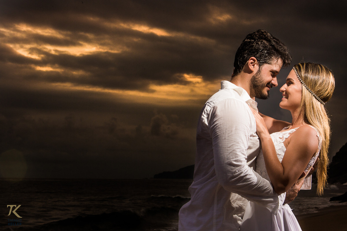 Casal se abraça enamorado ao entardecer na praia.