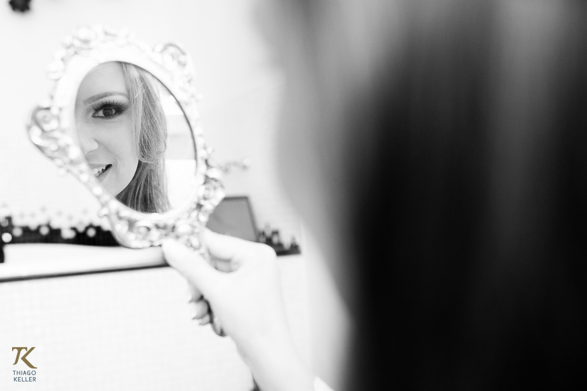Fotografia de casamento de Lívia e Paulo Henrique na cidade de Paracatu, Minas Gerais. Making off da noiva. Noiva se olhando no espelho. Foto em preto e branco.