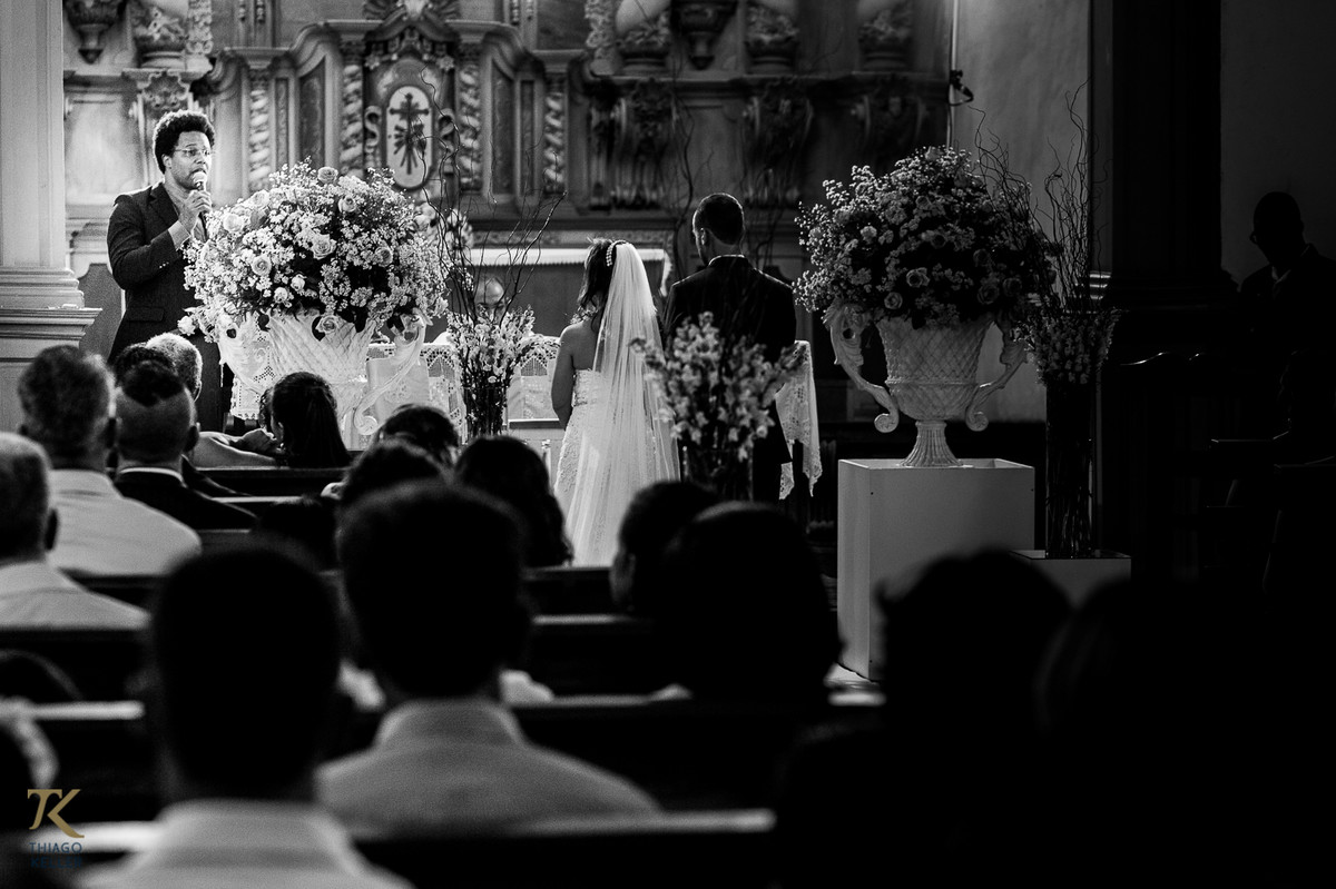 Fotografia de casamento de Lívia e Paulo Henrique na cidade de Paracatu, Minas Gerais. Casal ouve a liturgia na Igreja do Rosário. Foto em Preto e Branco.