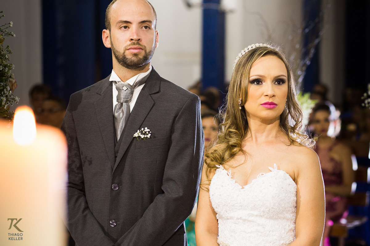 Fotografia de casamento de Lívia e Paulo Henrique na cidade de Paracatu, Minas Gerais. Noivos ouvem a liturgia durante a cerimônia.
