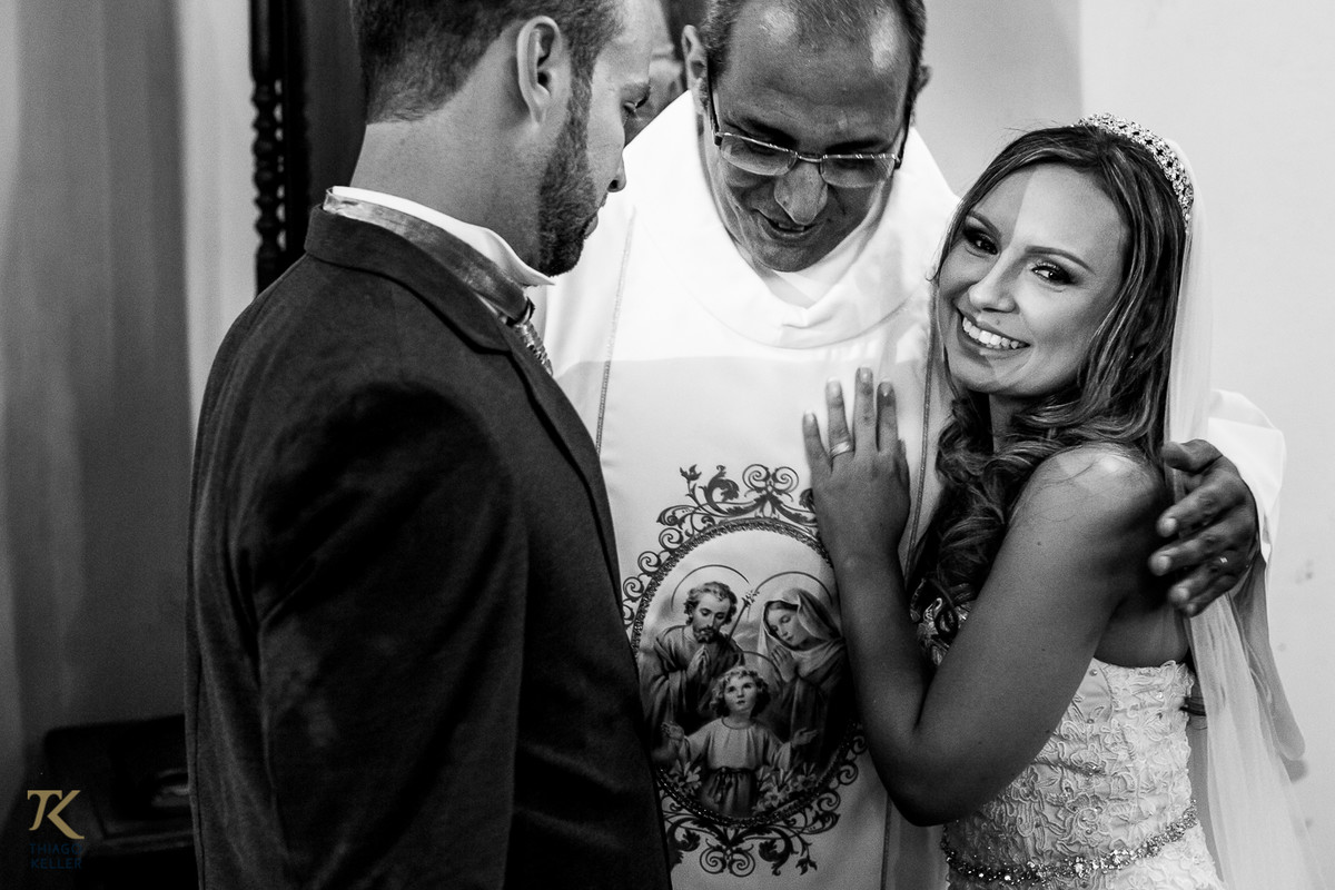 Casal é abraçado pelo padre que realizou a cerimônia.