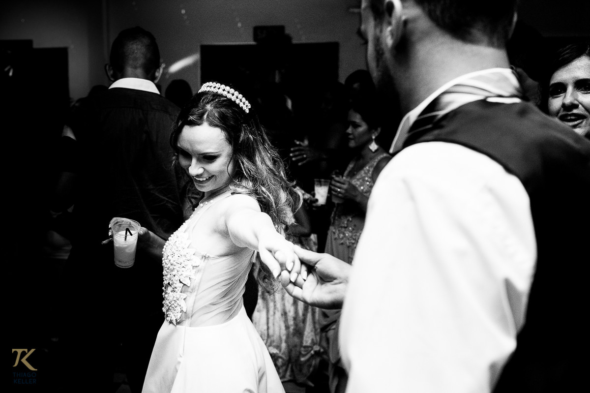 Fotografia de casamento de Lívia e Paulo Henrique na cidade de Paracatu, Minas Gerais. Noivos animados na pista de dança. Foto em preto e branco.
